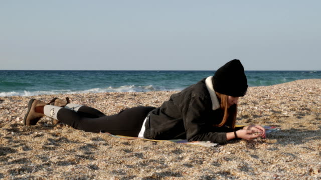 Chica-está-descansando-acostado-en-la-orilla-del-mar-Mediterráneo-en-un-día-frío-de-otoño