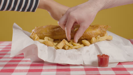 People-Using-Fingers-To-Eat-Traditional-British-Takeaway-Meal-Of-Fish-And-Chips