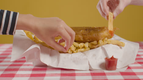 People-Using-Fingers-To-Eat-Traditional-British-Takeaway-Meal-Of-Fish-And-Chips-With-Ketchup