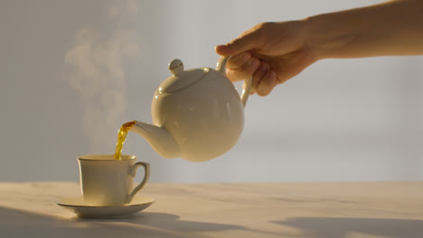 Studio-Shot-Of-Person-Making-And-Pouring-Traditional-British-Cup-Of-Tea-Using-Teapot