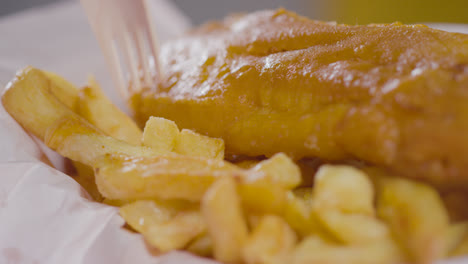 Close-Up-Of-Person-Eating-Traditional-British-Takeaway-Meal-Of-Fish-And-Chips-With-Wooden-Fork