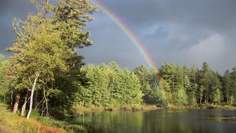 A-rainbow-over-a-forest-and-near-a-lake-in-Rural-Maine-