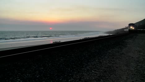 Beautiful-shot-of-an-Amtrak-train-passing-by-a-California-beach-at-sunset