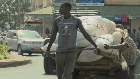 Männer-Arbeiten-Hart,-Um-In-Arusha,-Tansania,-Einen-Karren-Eine-Straße-Hinaufzuschieben