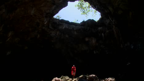 Spectacular-tilt-down-shot-of-a-Masai-warrior-stading-in-a-huge-pool-of-light-in-a-cave-in-Kenya