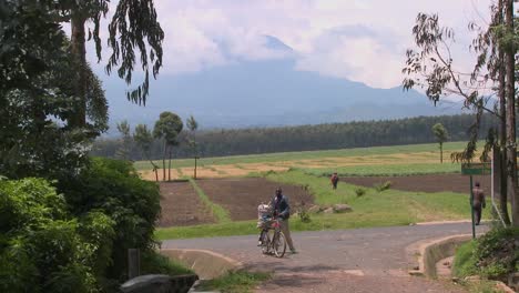 A-man-walks-his-bicycle-down-a-rural-road-in-Rwanda-with-the-Virunga-volcanos-in-the-background
