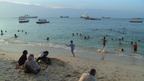 Children-play-and-swim-on-the-beach-in-Stone-Town-Zanzibar-at-sunset-while-sailboats-sail-in-the-distance