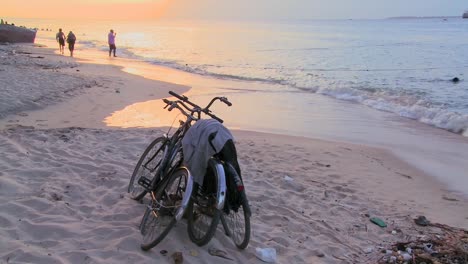 Sunset-shot-along-a-beach-with-two-bicycles-parked-on-the-shore-and-children-playing-in-distance