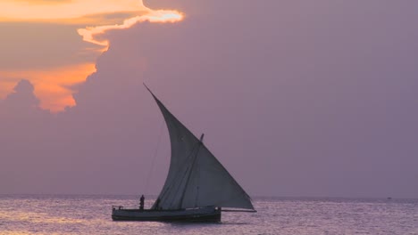 Eine-Schöne-Aufnahme-Eines-Dhow-Segelboots,-Das-Bei-Sonnenuntergang-Entlang-Der-Küste-Von-Sansibar-Segelt