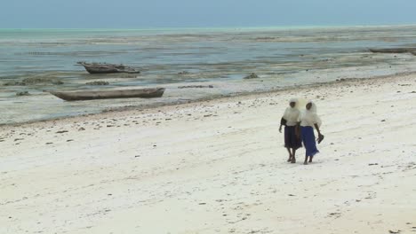 Two-Musulmán-girls-walk-in-school-outfits-along-a-white-sand-beach