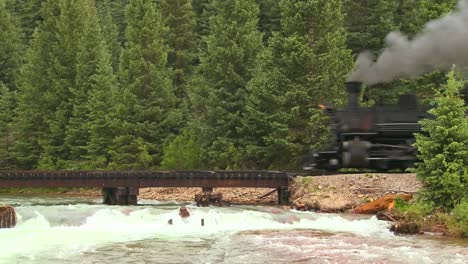 A-beautiful-shot-of-a-steam-train-crossing-a-bridge-over-a-roaring-río-in-the-Rocky-Mountains