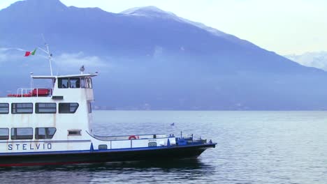 A-ferry-boat-arrives-at-a-beautiful-small-Italian-village-of-Bellagio-on-the-shores-of-Lake-Como-with-the-Italian-Alps-in-background