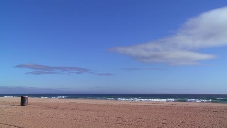 An-empty-beach-with-a-lone-garbage-can-and-blue-sky