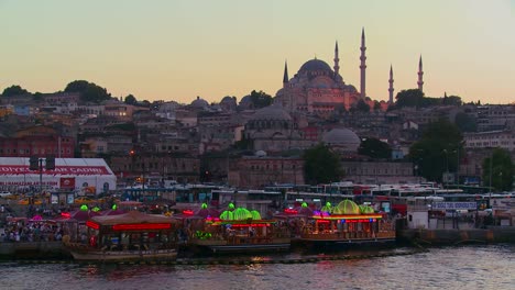 Colorful-boats-bob-in-the-water-at-dusk-in-front-of-a-mosque-in-Istanbul-Turkey
