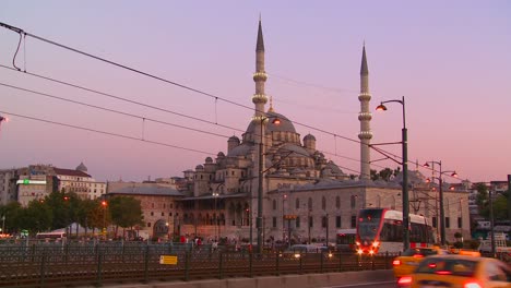Tranvías-De-Tránsito-Rápido-Y-El-Tráfico-Al-Anochecer-En-Frente-De-Una-Mezquita-En-Estambul,-Turquía