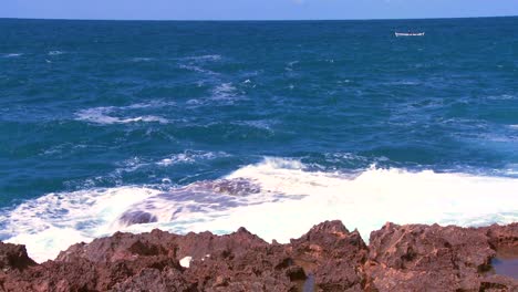 Wide-shot-of-waves-breaking-on-the-shoreline-with-a-small-fishing-boat-distant