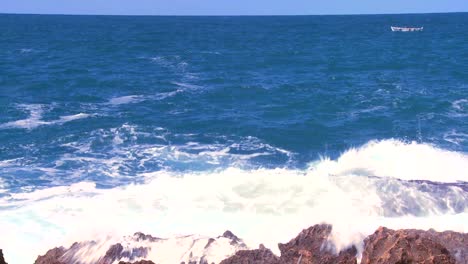 Wide-shot-of-waves-breaking-on-the-shoreline-with-a-small-fishing-boat-distant-1