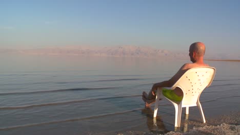 A-man-sits-on-a-plastic-chair-beside-the-Dead-Sea-in-Israel