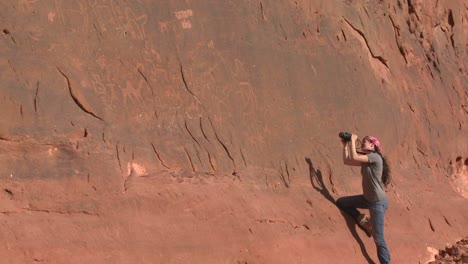 Una-Mujer-Fotografía-Petroglifos-Antiguos-Y-Misteriosos-Que-Representan-A-Humanos-Y-Camellos-En-El-Desierto-De-Arabia,-Cerca-De-Wadi-Rum,-Jordania.