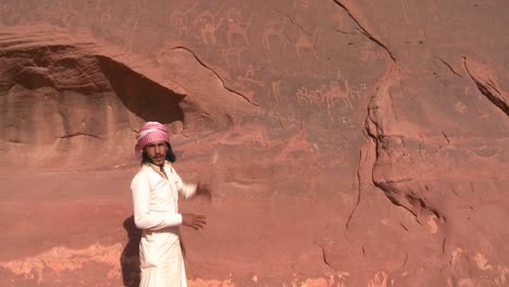 A-traditional-Bedouin-points-out-ancient-and-mysterious-petroglyphs-depict-humans-and-camels-in-the-Saudi-desert-near-Wadi-Rum-Jordan