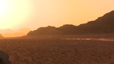 A-trail-of-dust-follows-a-vehicle-into-the-sunset-across-the-desert-in-Wadi-Rum-Jordan