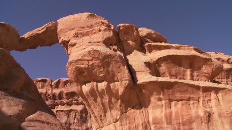 Schwenken-Sie-Hinüber-Zu-Einer-Erstaunlichen-Bogenformation-In-Der-Sadi-Wüste-Im-Wadi-Rum-Jordanien,-Während-Ein-Beduinenmann-Durchläuft?
