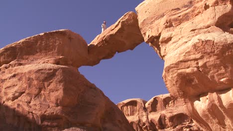 Eine-Erstaunliche-Bogenformation-In-Der-Sadi-Wüste-Im-Wadi-Rum-Jordanien-Mit-Einem-Beduinenmann,-Der-Durchgeht?