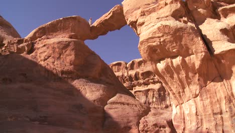Tilt-up-to-an-amazing-arch-formation-in-the-Sadi-desert-in-Wadi-Rum-Jordan-with-a-Bedouin-man-walking-through
