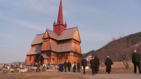 People-in-traditional-clothing-walk-towards-an-old-wooden-stave-church-in-Norway-1