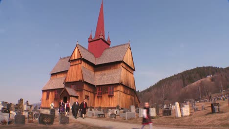 People-in-traditional-clothing-walk-towards-an-old-wooden-stave-church-in-Norway-2