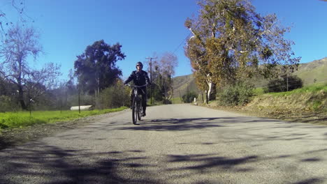 A-man-rides-a-motorized-bicycle-through-the-countryside-on-a-two-lane-road-1