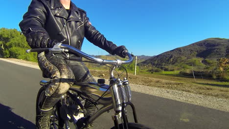 A-leather-clad-man-rides-a-motorized-bicycle-through-the-countryside-on-a-two-lane-road-1