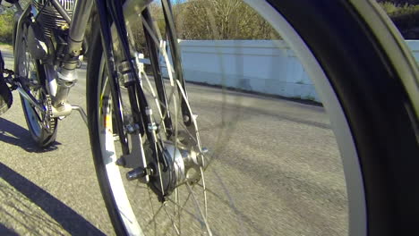 Close-up-of-the-wheels-of-a-motorized-bicycle-through-the-countryside-on-a-two-lane-road