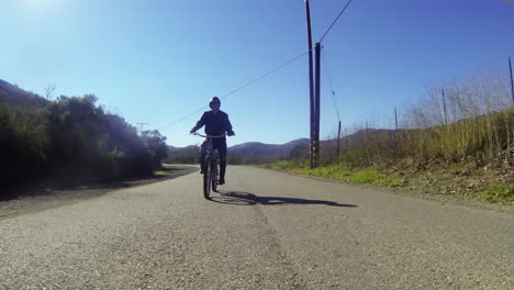 Un-Hombre-Vestido-De-Cuero-Monta-Una-Bicicleta-Motorizada-Por-El-Campo-En-Una-Carretera-De-Dos-Carriles-2
