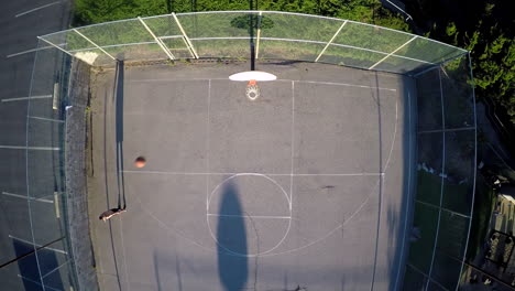 A-birds-eye-aerial-over-a-basketball-player-shooting-baskets-on-an-outdoor-court