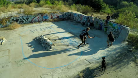 Toma-Aérea-De-Muchachos-Adolescentes-En-Patineta-En-Los-Cimientos-Cubiertos-De-Graffiti-De-Un-Edificio-Abandonado-3