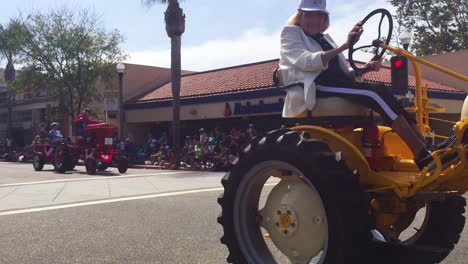 Una-Anciana-Granjera-Conduce-Su-Tractor-Por-Una-Calle-De-La-Ciudad-Durante-Un-Desfile-Del-4-De-Julio-En-Una-Pequeña-Ciudad