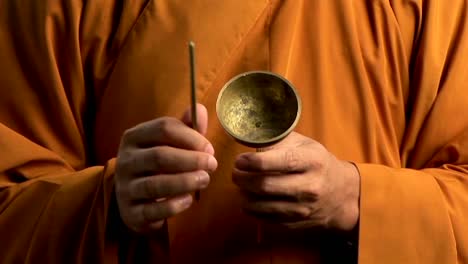 A-Buddhist-monk-wearing-an-orange-robe-taps-a-bell-with-a-small-stick-1