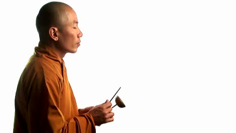 A-Buddhist-monk-wearing-an-orange-robe-taps-a-bell-with-a-small-stick-2