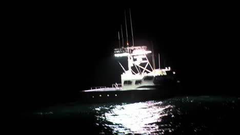 A-boat-sits-in-the-water-at-night-while-a-man-works-on-the-deck
