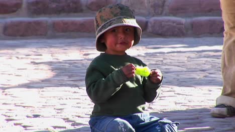 A-Latin-American-boy-sits-on-the-ground-and-eats-a-green-popsicle-in-a-South-American-village