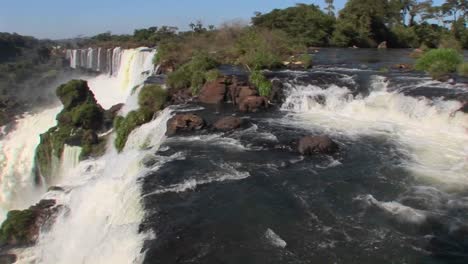 Pan-across-Iguacu-Falls-flowing-out-of-the-jungle-with-a-rainbow-foreground