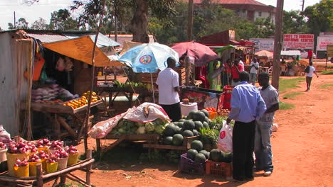 People-buy-produce-at-stands-cars-pass-by-on-the-street