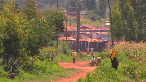 People-in-a-small-village-walk-down-a-red-dirt-road