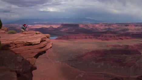 Ein-Fotograf-Geht-Zu-Einem-Felsvorsprung,-Der-Tagsüber-Ein-Tal-Von-Tafelbergen-Im-Canyonlands-Nationalpark-In-Utah-überblickt