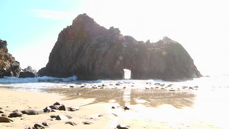 Waves-roll-into-shore-on-a-sunny-day-along-California-coastline-with-an-arch-rock-foreground