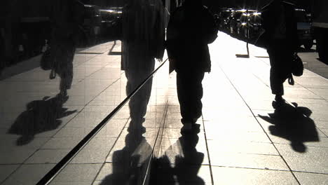 Pedestrians-are-silhouetted-as-they-pass-along-a-sidewalk-in-a-city-