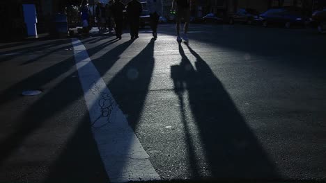 Pedestrians-pass-in-a-crosswalk-on-a-busy-city-street-as-long-shadows-stretch-along-the-pavement-