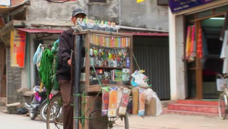 Un-Hombre-Pedalea-Una-Bicicleta-Cargada-Con-Medicamentos-Y-Otros-Bienes-Por-Una-Calle-Estrecha-En-Vietnam