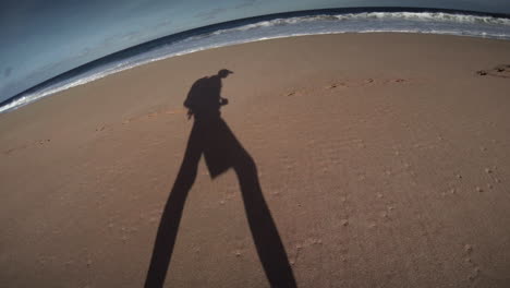 Der-Schatten-Eines-Mannes-Geht-Mit-Einem-Rucksack-Am-Strand-Entlang